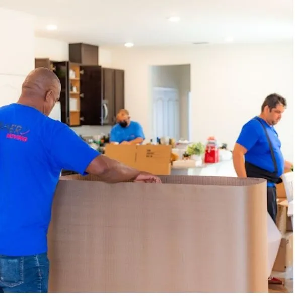 Granero Moving crew members in blue company t-shirts wrapping furniture in a home